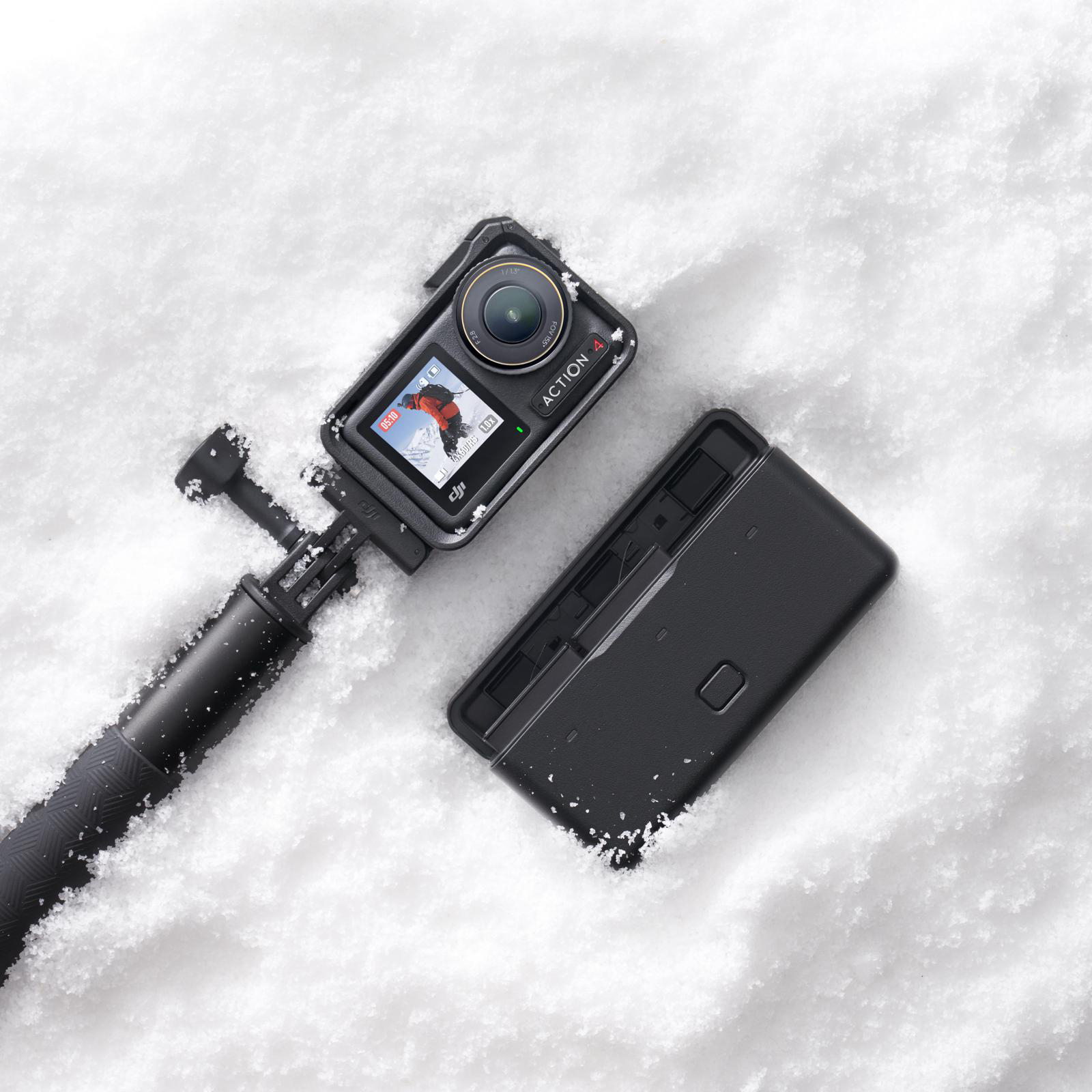 Eine Actionkamera mit einem Stock im Schnee neben einem schwarzen Gehäuse. Der Bildschirm zeigt einen Skifahrer.