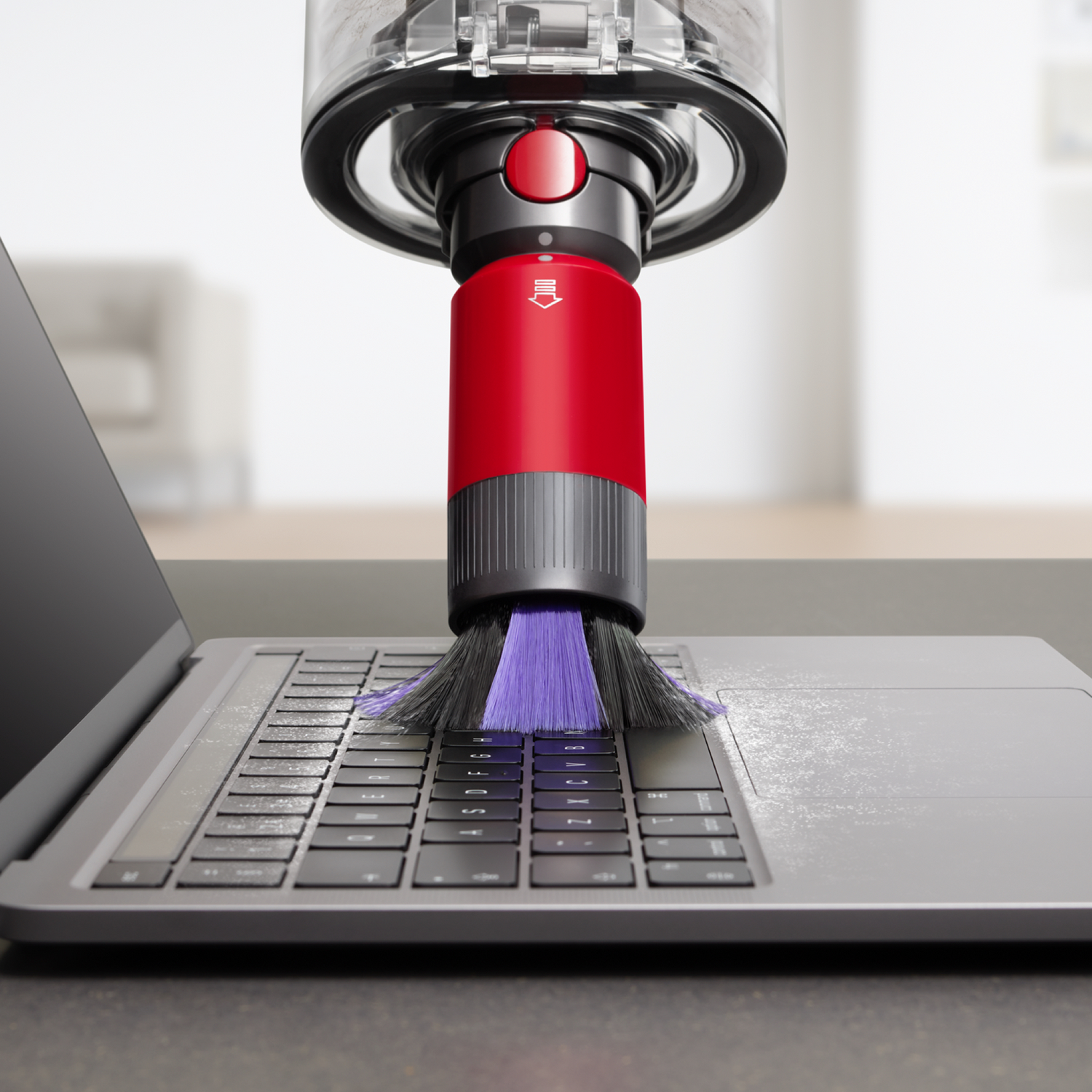 Een rode stofzuigerkop maakt een laptoptoetsenbord schoon.