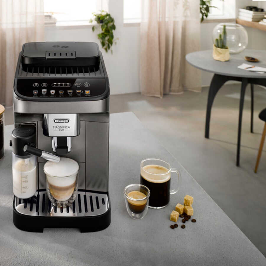 Bir masada kahve fincanları ve kahve çekirdekleri ile espresso makinesi. Arka planda bir kişi.