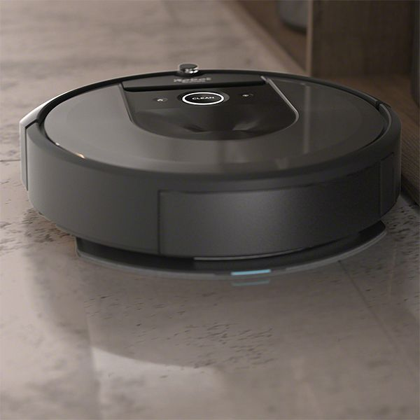 Un aspirateur robot noir sur un sol en pierre. L'aspirateur est près d'un meuble en bois.