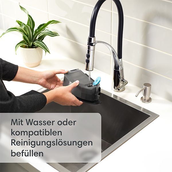 Personne remplissant un récipient noir d'eau à l'évier. Plante et robinet en arrière-plan.