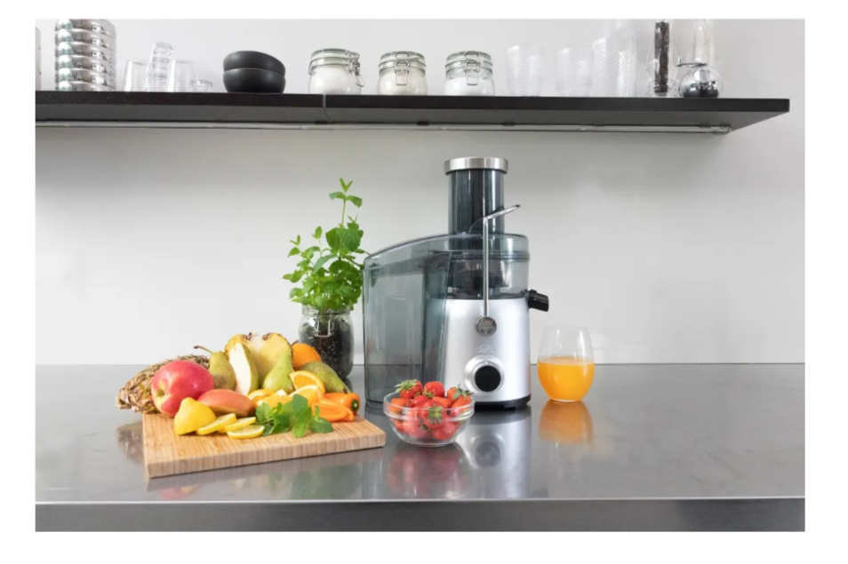 Centrifugeuse et fruits sur un plan de travail. Comprend des pommes, du citron et des fraises, avec un verre de jus.