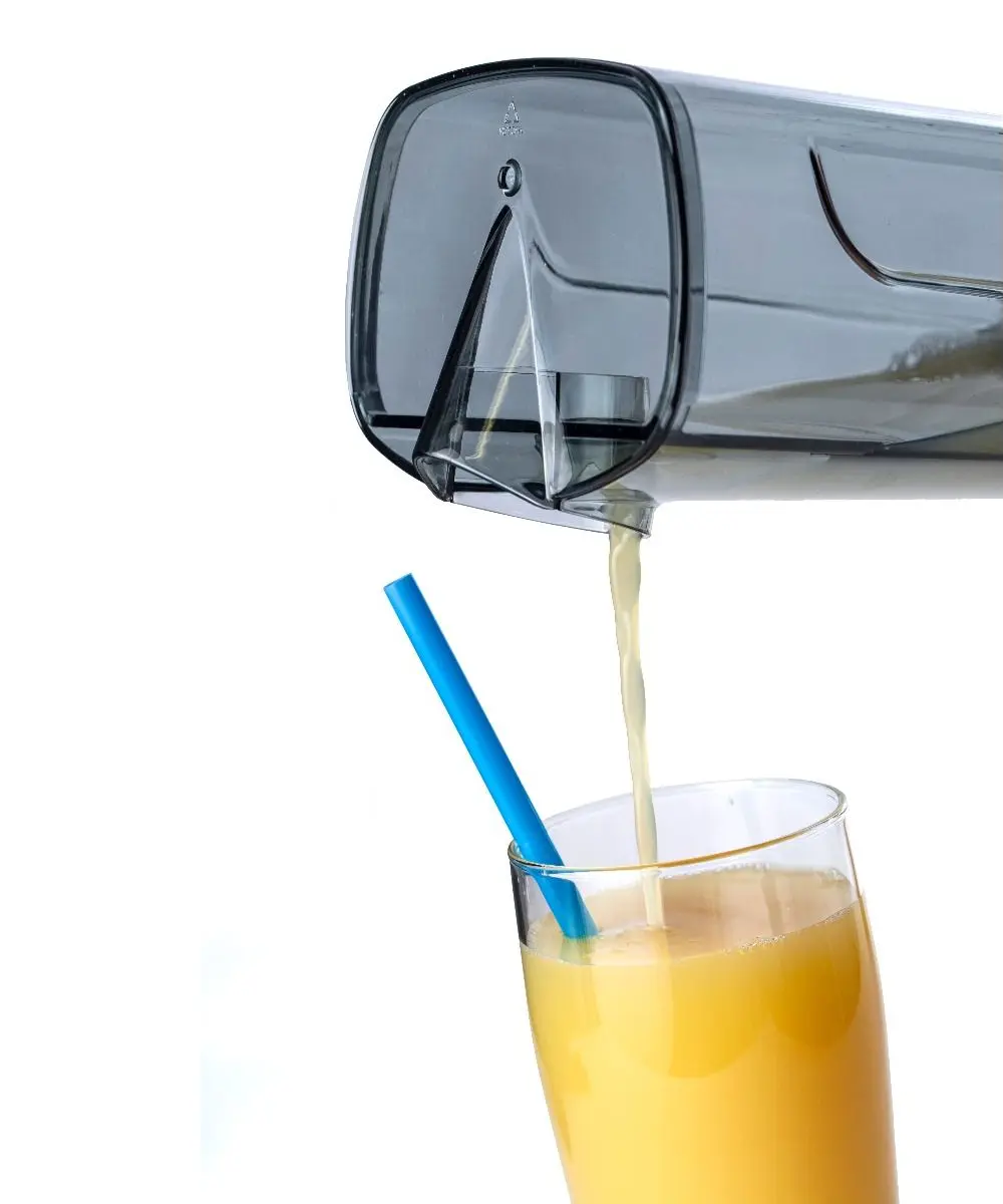 Un récipient transparent verse du jus d'orange dans un verre. Une paille bleue est dans le verre.
