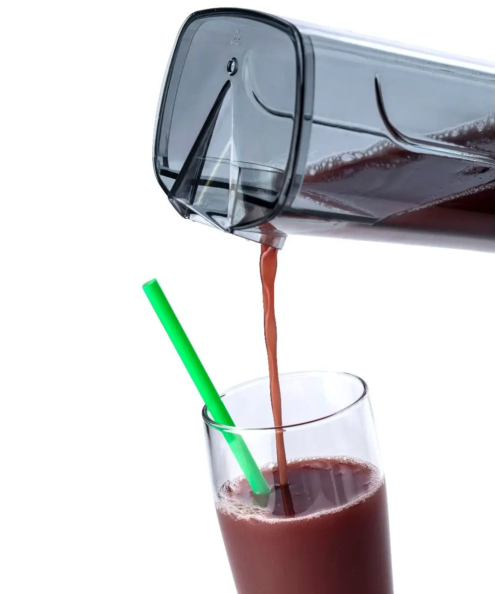 Une carafe transparente verse un liquide rouge foncé dans un grand verre avec une paille verte.