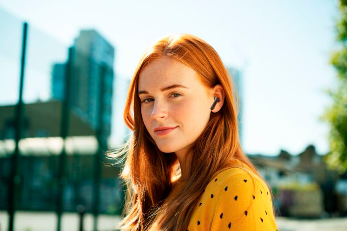 Une femme rousse portant une chemise jaune à pois noirs avec un écouteur sans fil.
