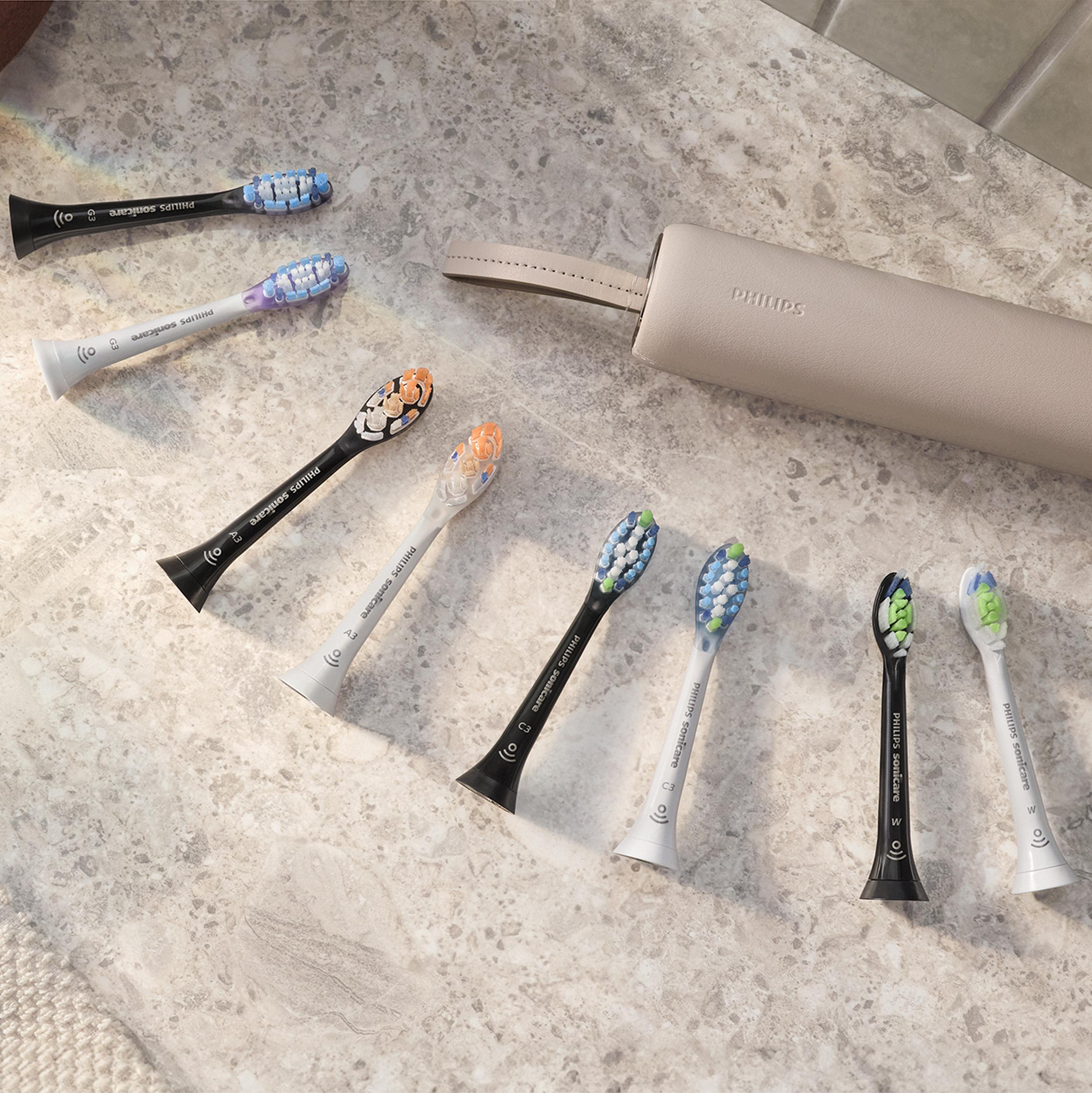 Verschiedene Philips Sonicare Zahnbürstenköpfe und ein beiges Reiseetui sind auf einer Steinoberfläche angeordnet.