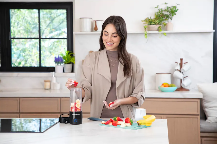 Femme préparant un smoothie. Elle met des fruits dans un blender. Cadre de cuisine, fruits sur le comptoir.