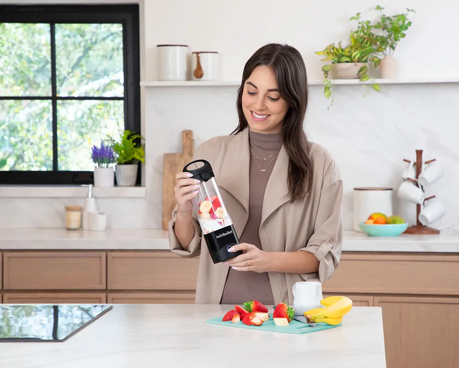 Une femme dans une cuisine préparant un smoothie avec un mixeur portable.