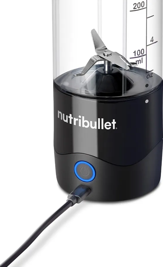 Un blender Nutribullet noir avec un récipient transparent indiquant les mesures, et un câble de charge noir branché.