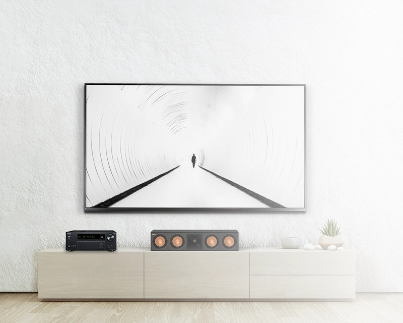 Living room setup: TV on white wall, soundbar and receiver on a white cabinet.