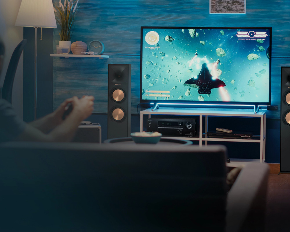 Man playing a video game on TV, surrounded by speakers and a sofa.