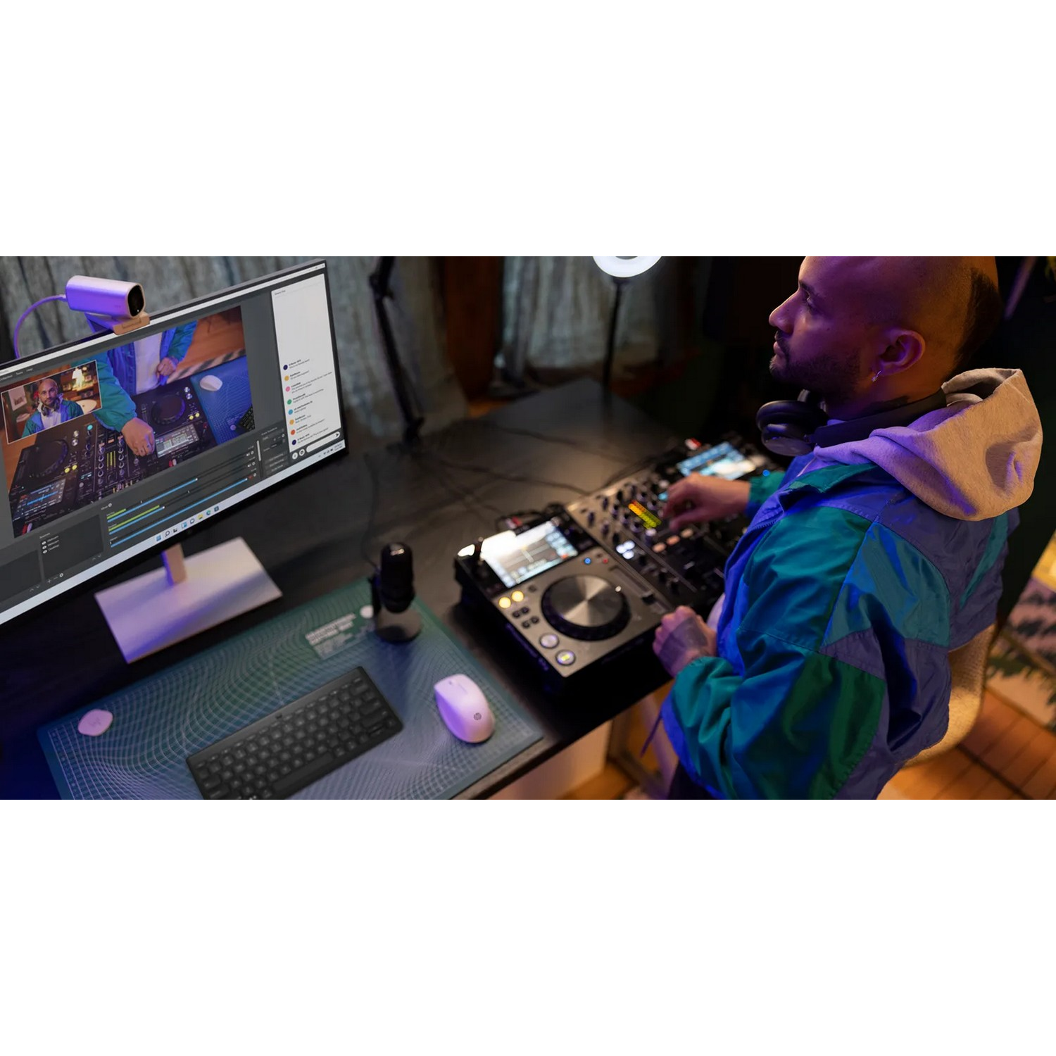 A DJ in a studio mixing music. He's in front of a computer screen and a mixing board.