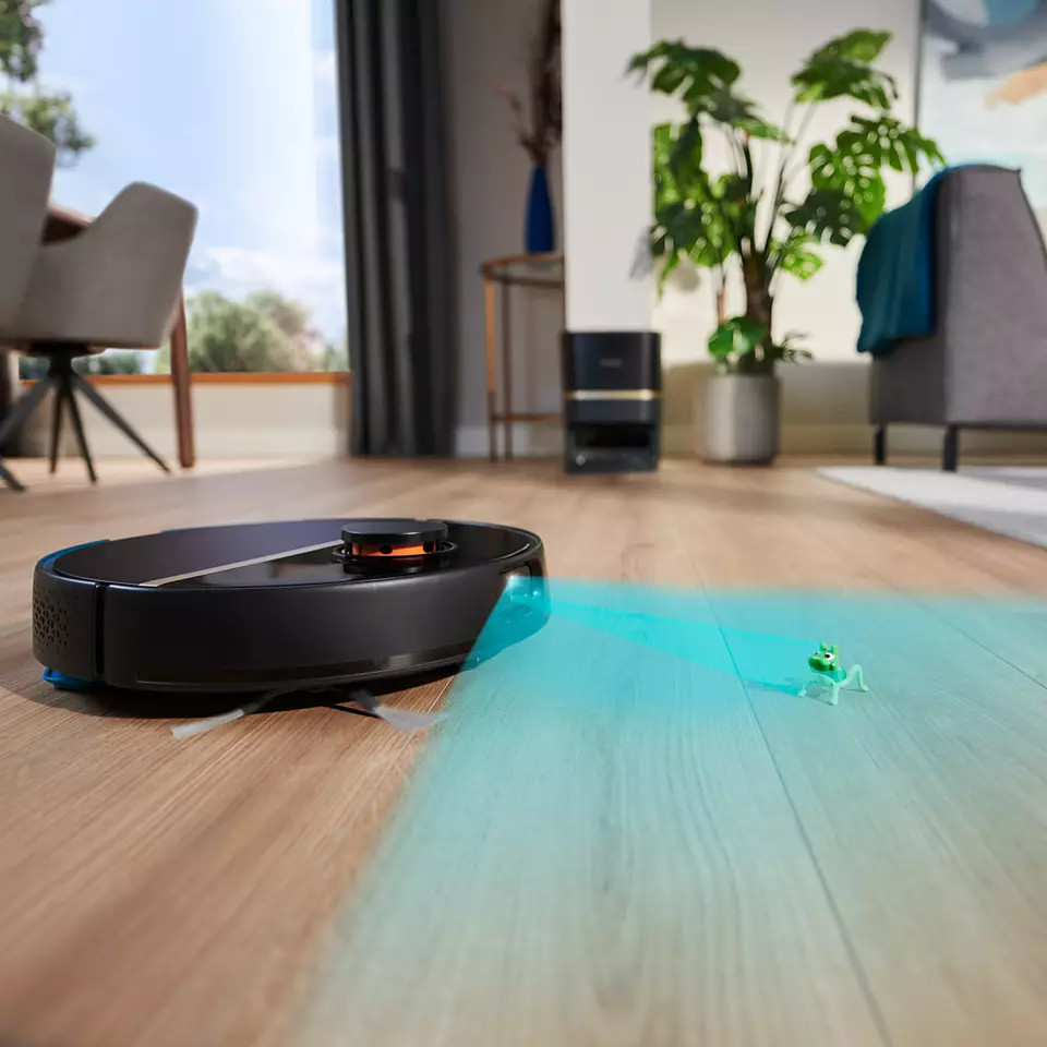 Zwarte robotstofzuiger op een houten vloer. Blauw licht uitgestraald. Een speelgoedkikker op de vloer.