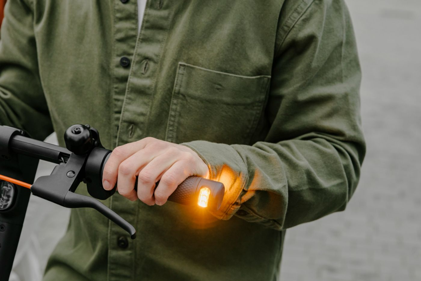 Person hält Lenker eines Rollers. Das Licht des Rollers leuchtet. Grüne Jacke.