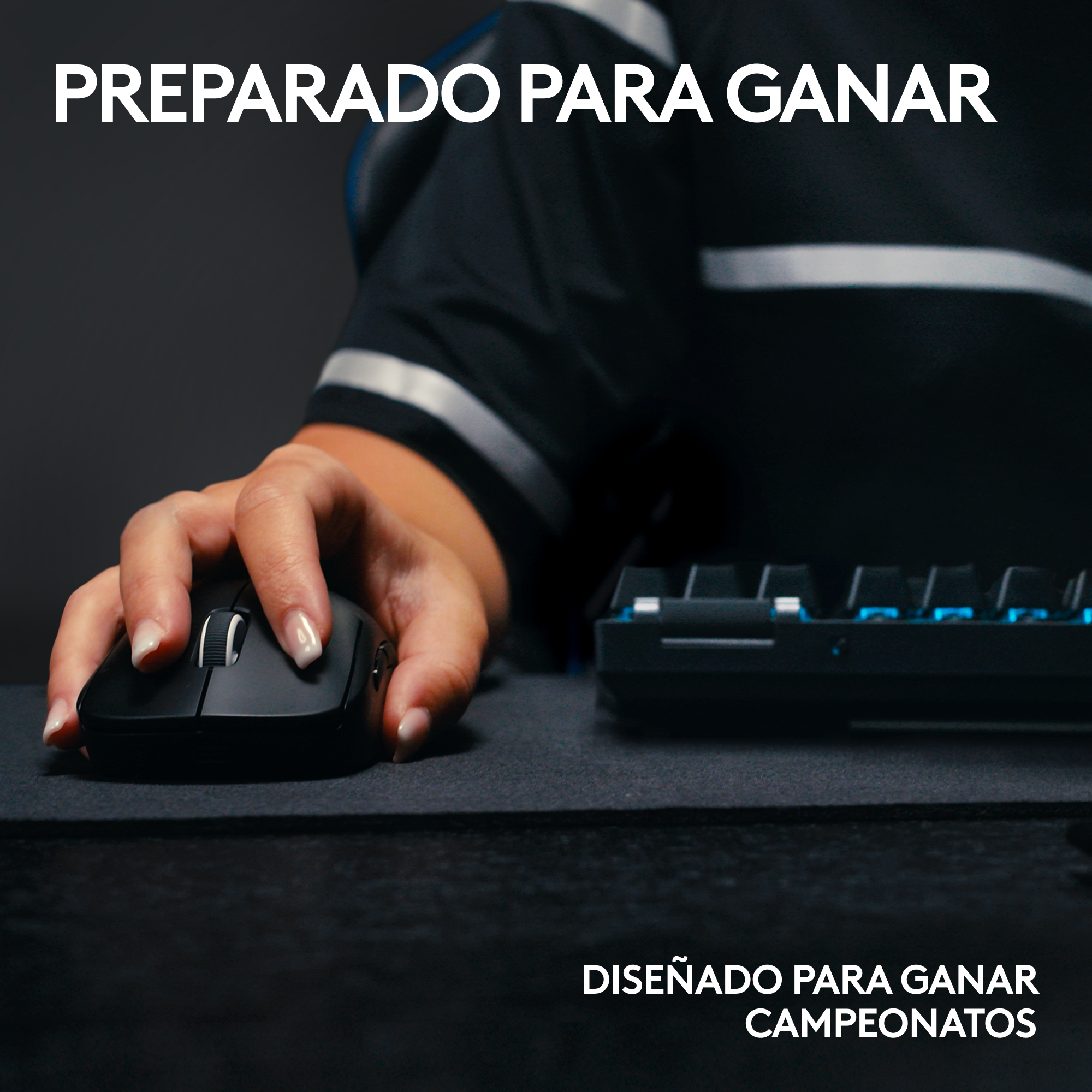 Mano usando un ratón negro en una alfombrilla negra, con un teclado al fondo.