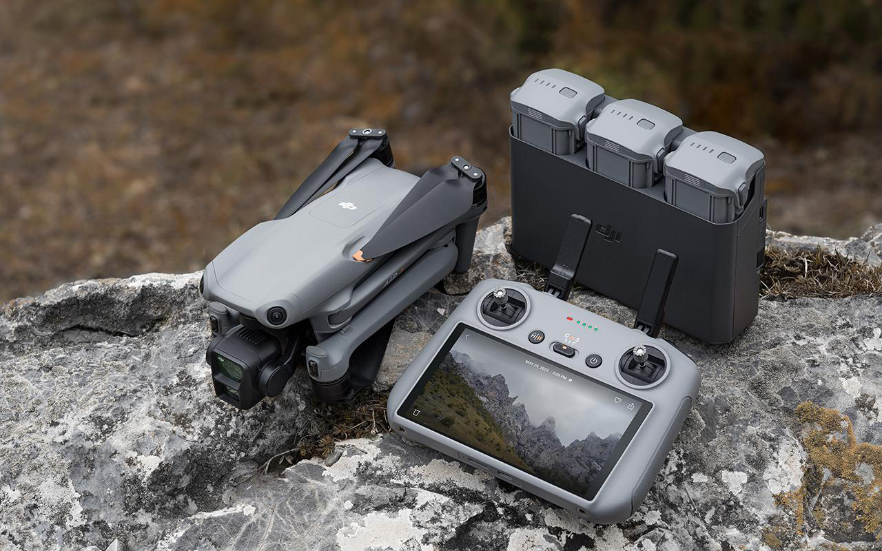 Drohne mit Controller und drei Akkus auf Felsen. Landschaft im Hintergrund.