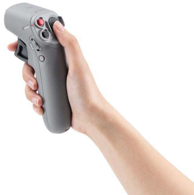 Ręka trzymająca szary kontroler drona z przyciskami i spustem.