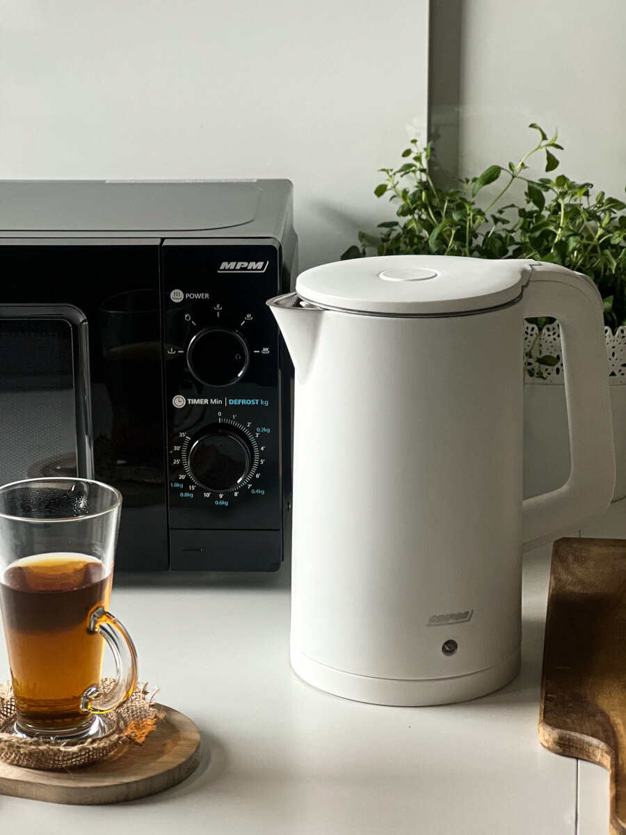 Biały czajnik i kuchenka mikrofalowa na białym blacie. Szklanka herbaty po lewej.