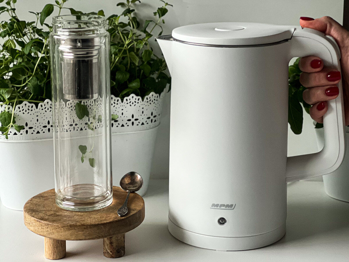 Kobieta trzymająca biały czajnik elektryczny i zestaw do herbaty.