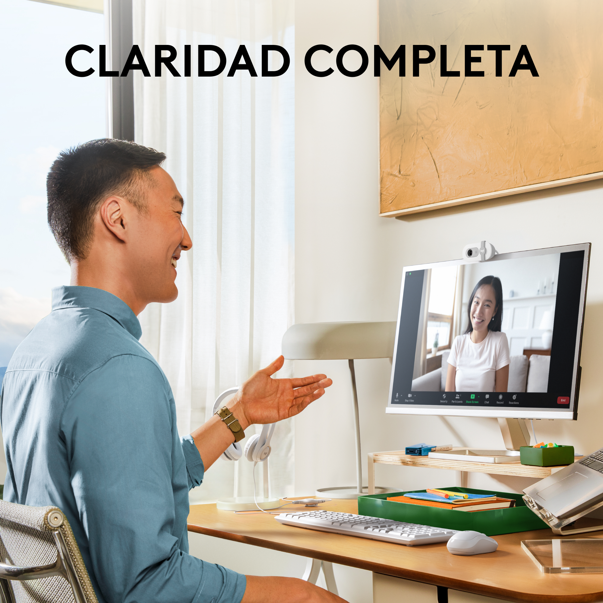 Hombre con camisa azul en videollamada. Monitor blanco y portátil en la escena.