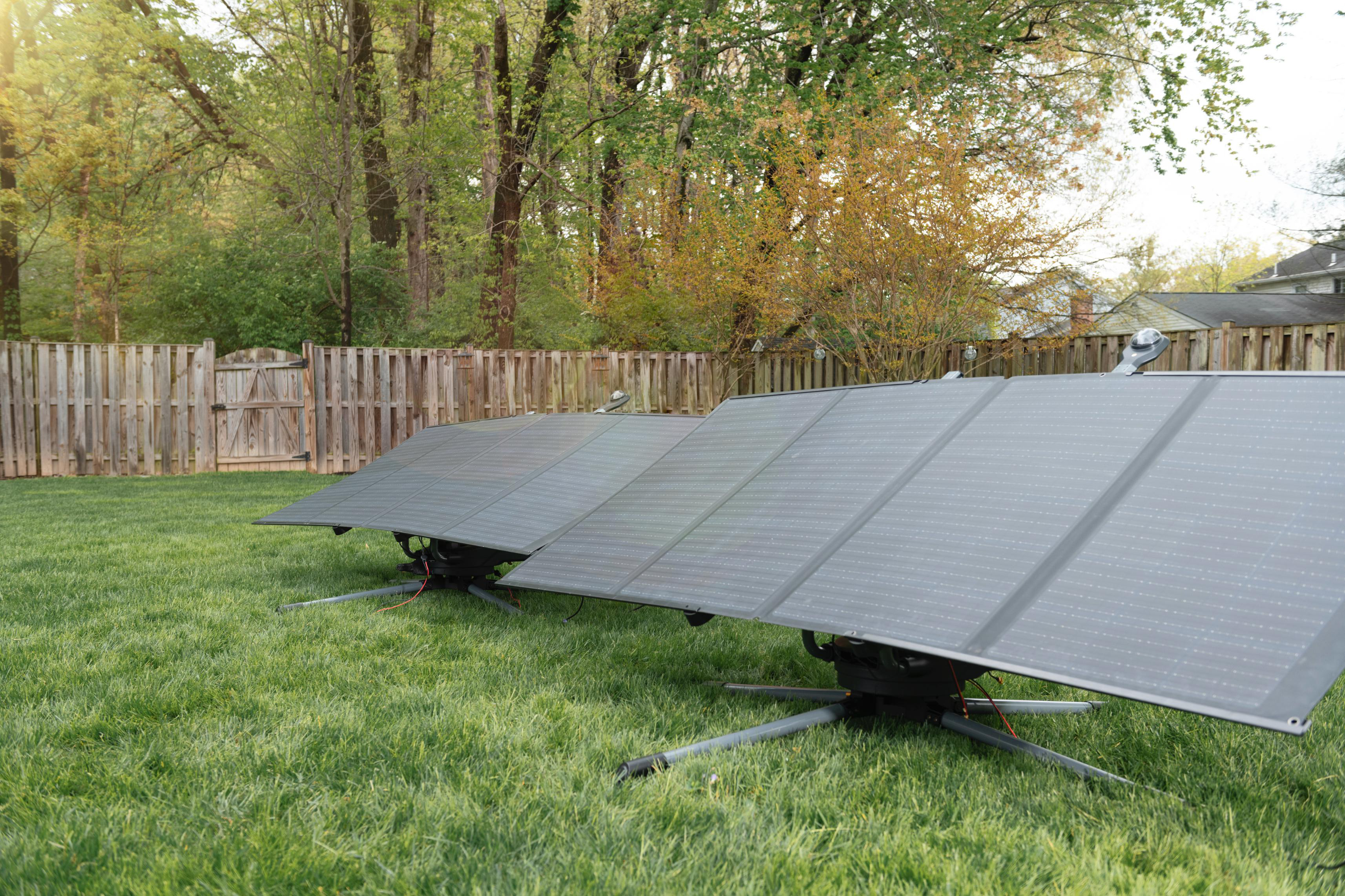 Solarpaneele in einem grasbewachsenen Garten, Holzzaun und Bäume im Hintergrund.
