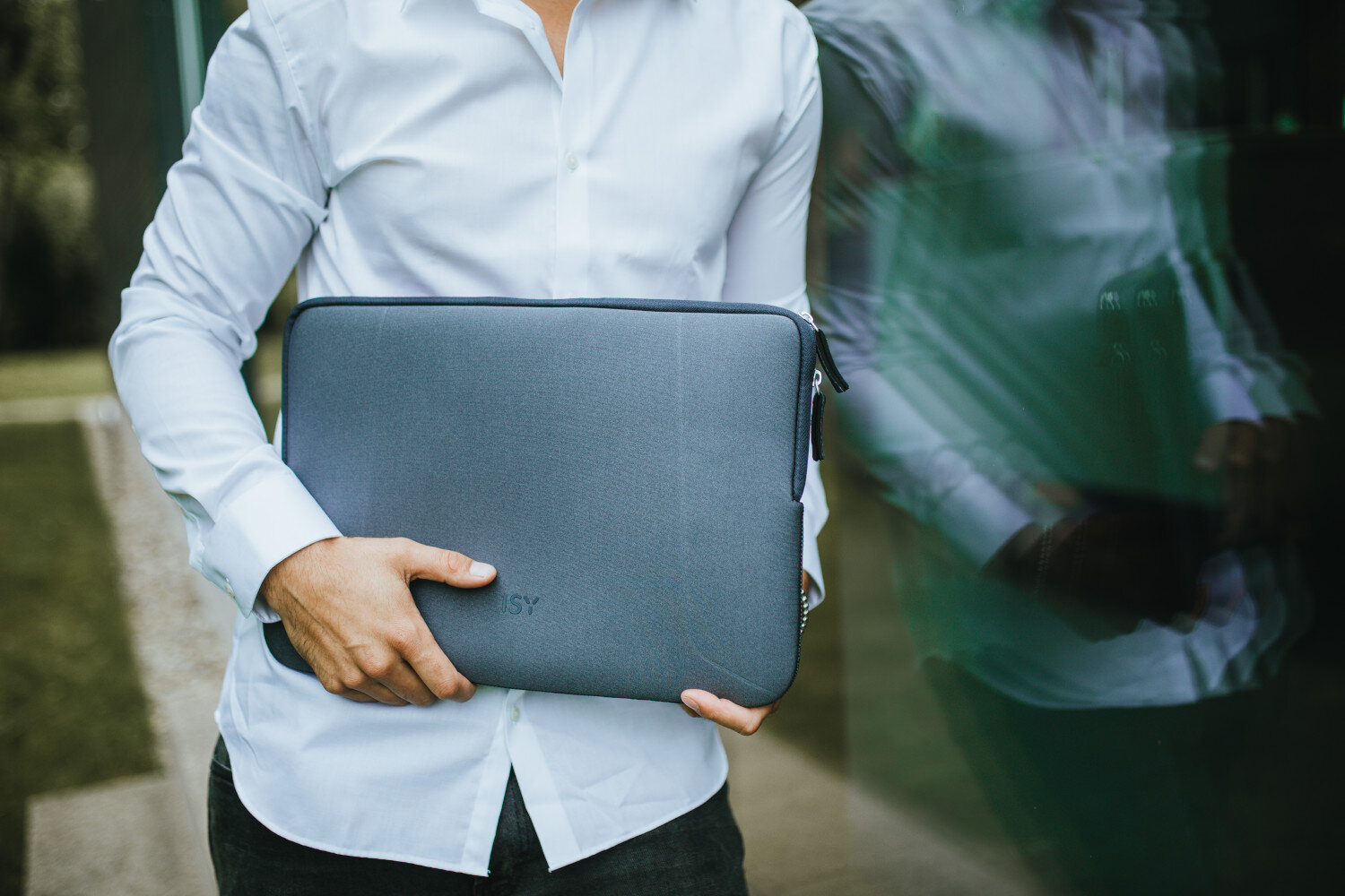Osoba trzymająca szare etui na laptopa, z odbiciem budynku w tle.
