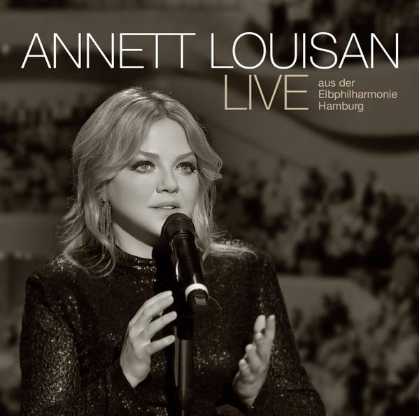 Annett Louisan Live Albumcover. Eine Frau singt in ein Mikrofon. Der Hintergrund ist ein verschwommener Konzertsaal.