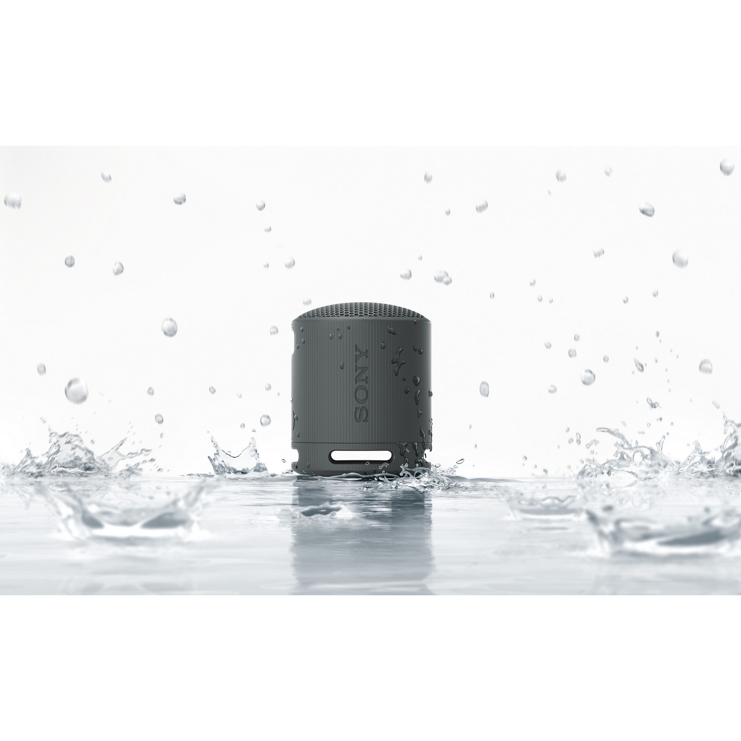 Haut-parleur portable gris dans l'eau, avec des gouttelettes d'eau autour.