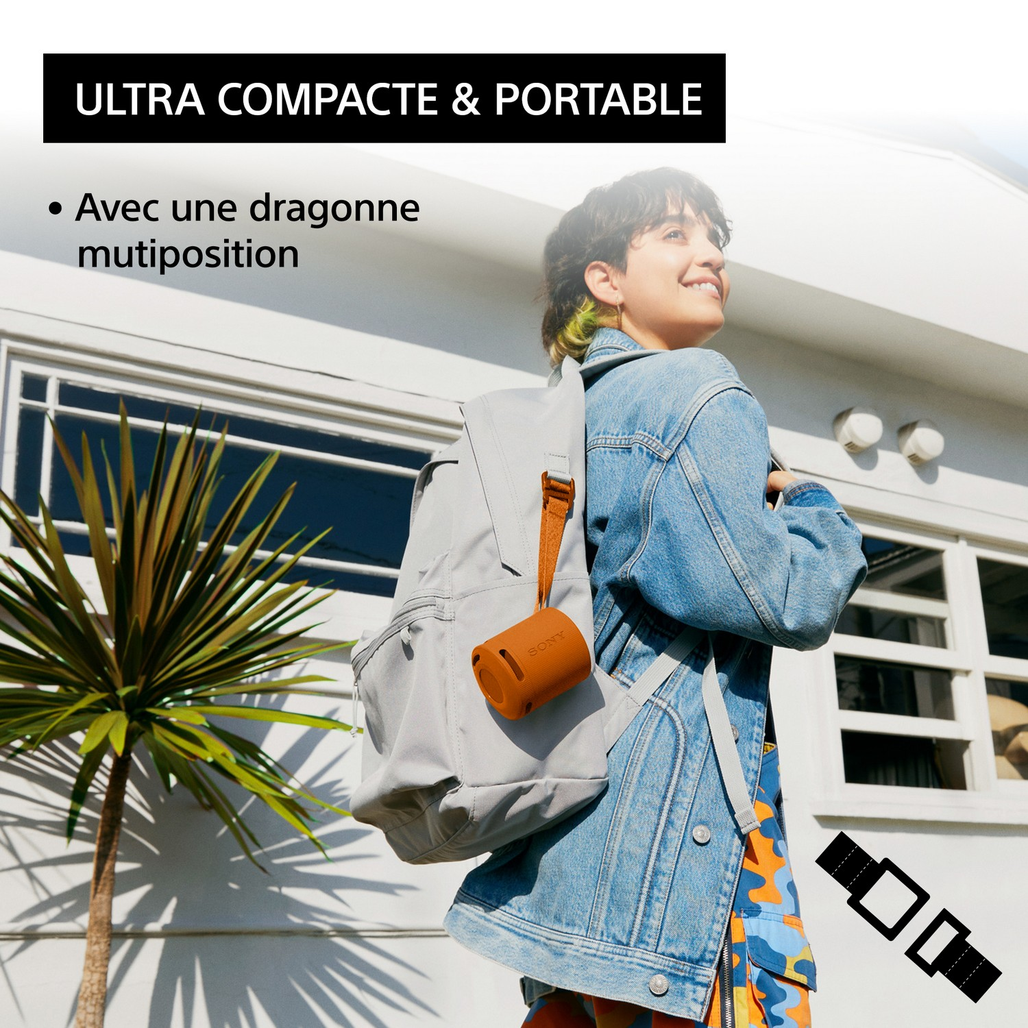 Une femme portant une veste en jean tient un haut-parleur marron attaché à un sac à dos gris. Texte en français.