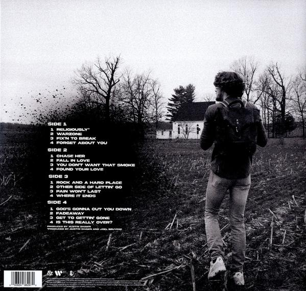 Mann steht mit Rucksack, Blick nach hinten, auf ein Gebäude zu. Vinylalbumcover mit Titelliste.