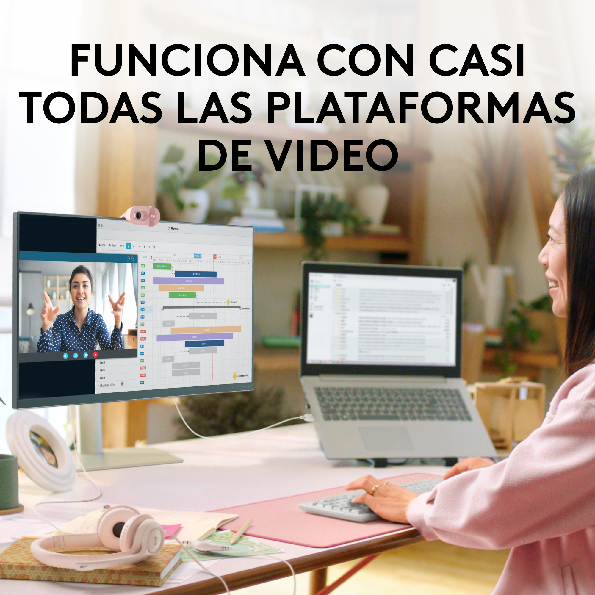 Mujer videollamando en un monitor, con webcam rosa y accesorios rosas en un escritorio. Portátil.