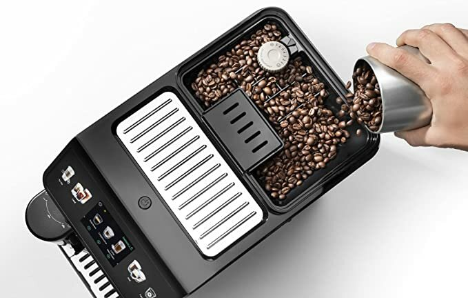 Czarny ekspres do kawy z ziarnami kawy w pojemniku i ręką wsypującą ziarna.