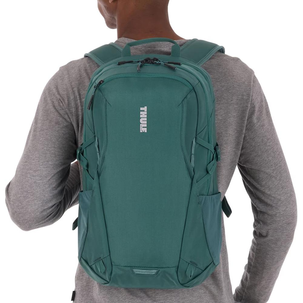 Teal renkli sırt çantası takan adam, Thule logosu görünür, beyaz arka plan üzerinde.
