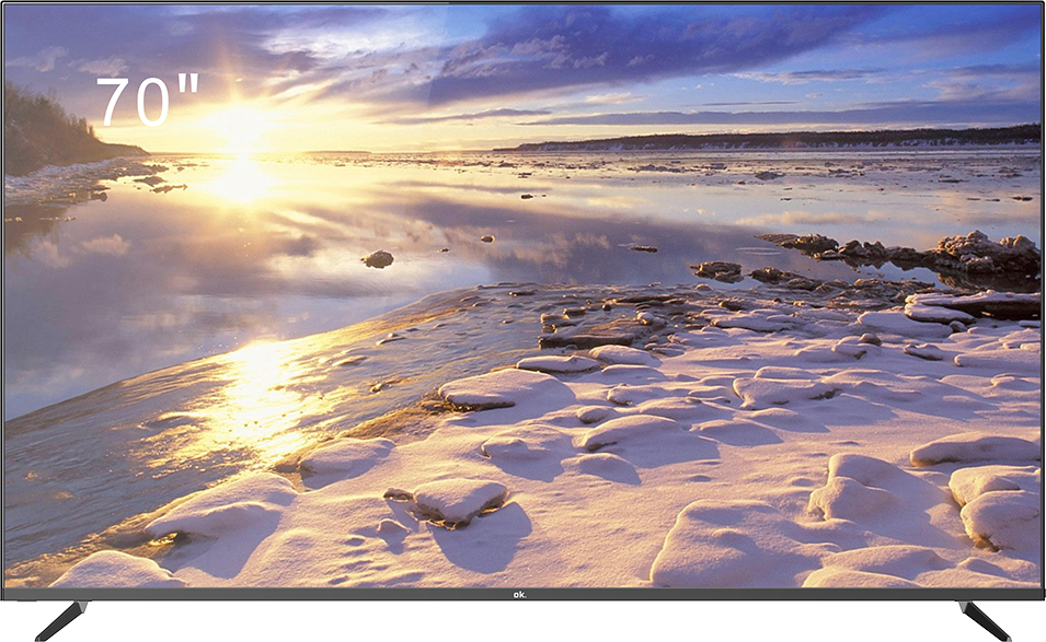 Ein 70"-Fernseher zeigt eine Winterszene. Schneebedeckter Vordergrund, Wasser und Sonnenuntergang mit Wolken. Der Fernseher hat einen schwarzen Rahmen und Beine.