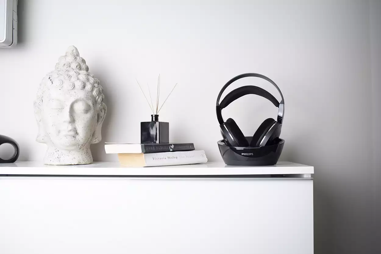 Weißes Regal mit Buddha-Kopf, Büchern, schwarzem Diffusor und schwarzen Kopfhörern auf Ständer.