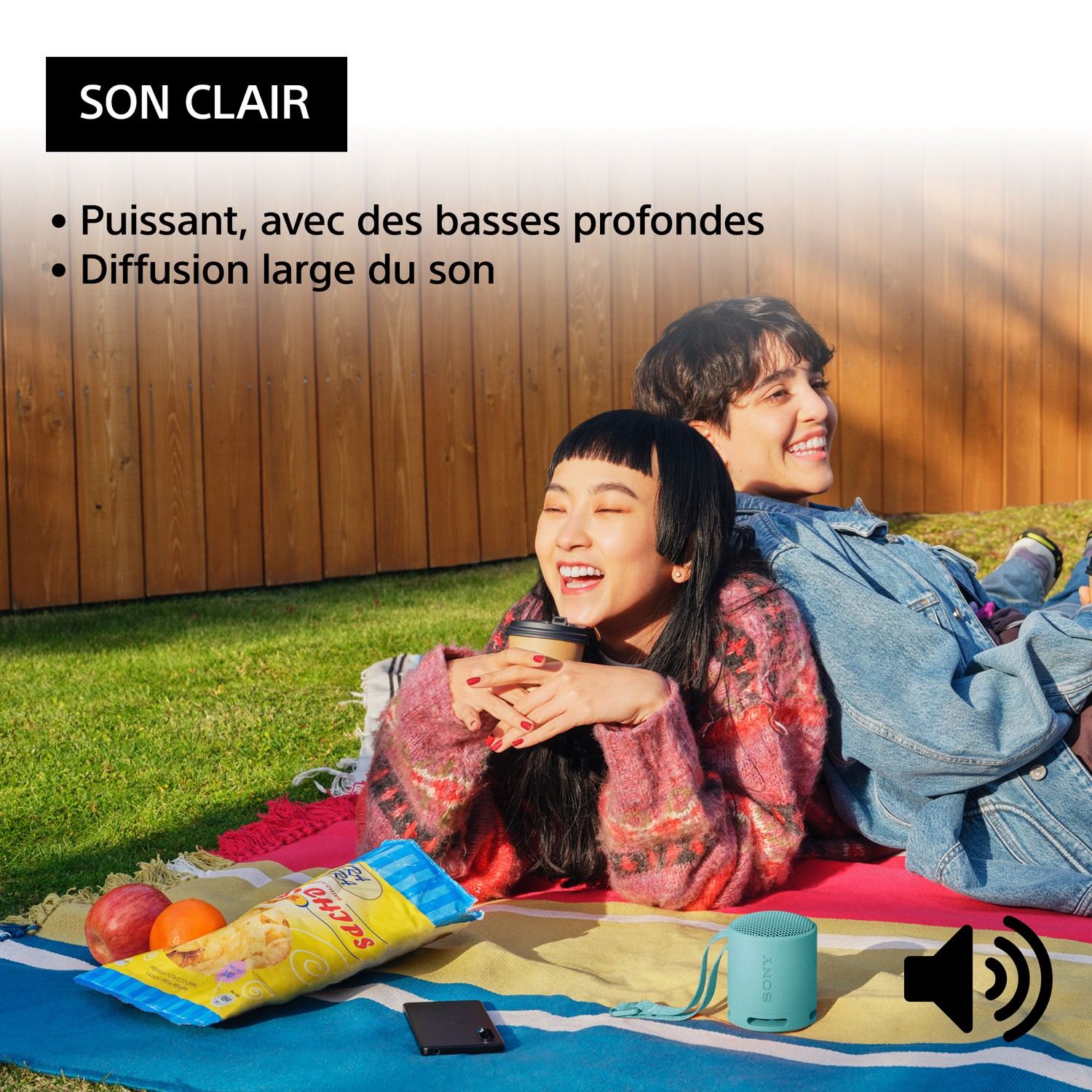 Deux personnes souriantes, avec un haut-parleur, des chips et un téléphone.