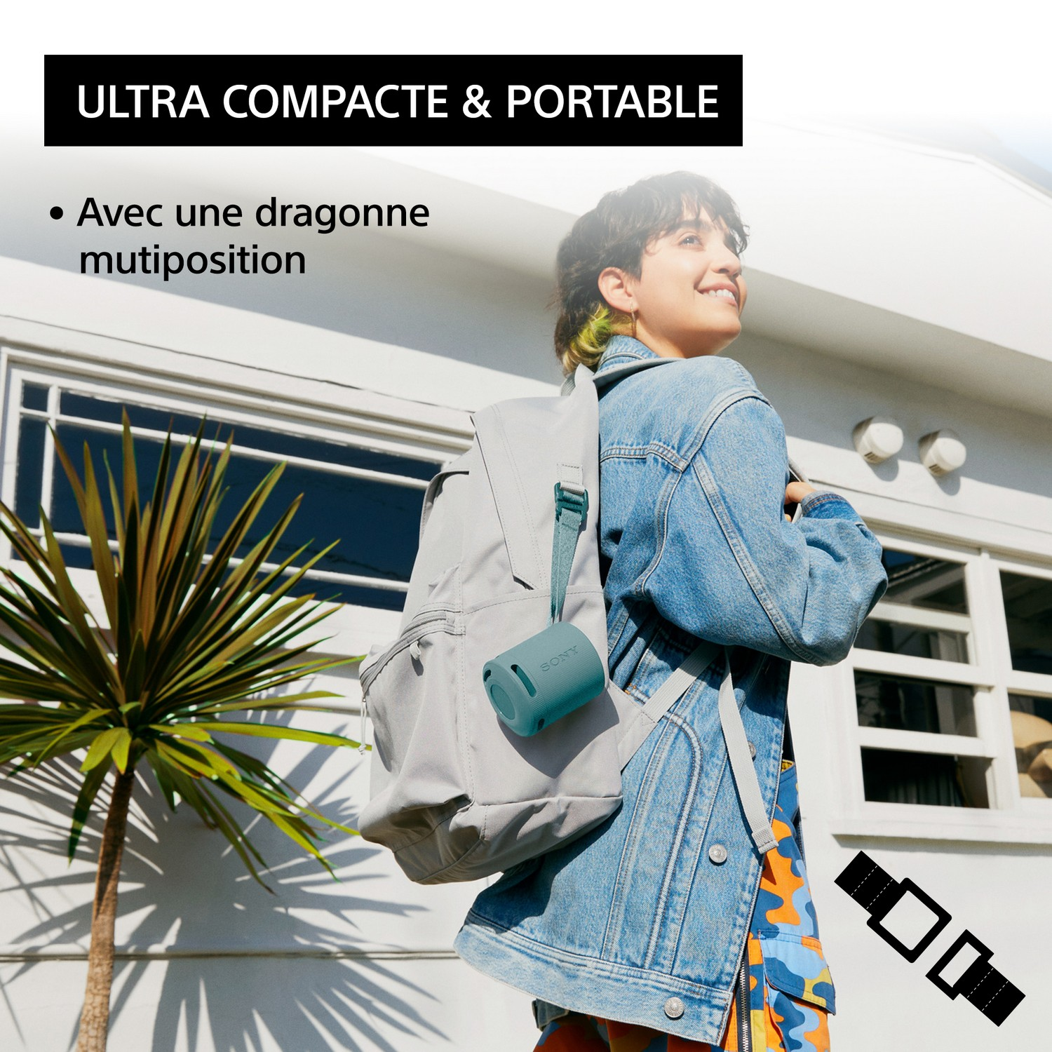 Femme avec un haut-parleur vert-bleu sur son sac à dos, souriant dehors.