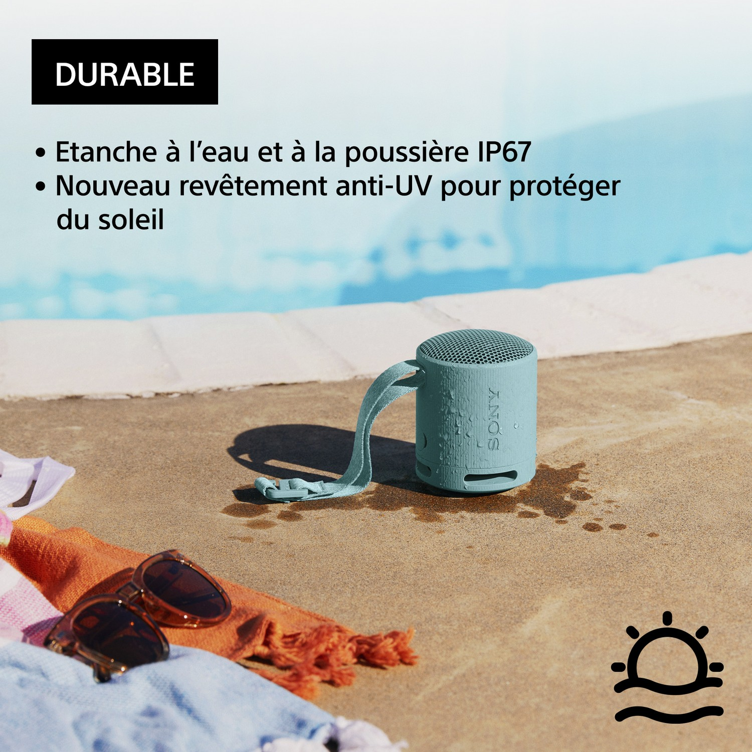 Haut-parleur bleu près d'une piscine. Lunettes de soleil et serviette visibles. Durable, protection solaire.