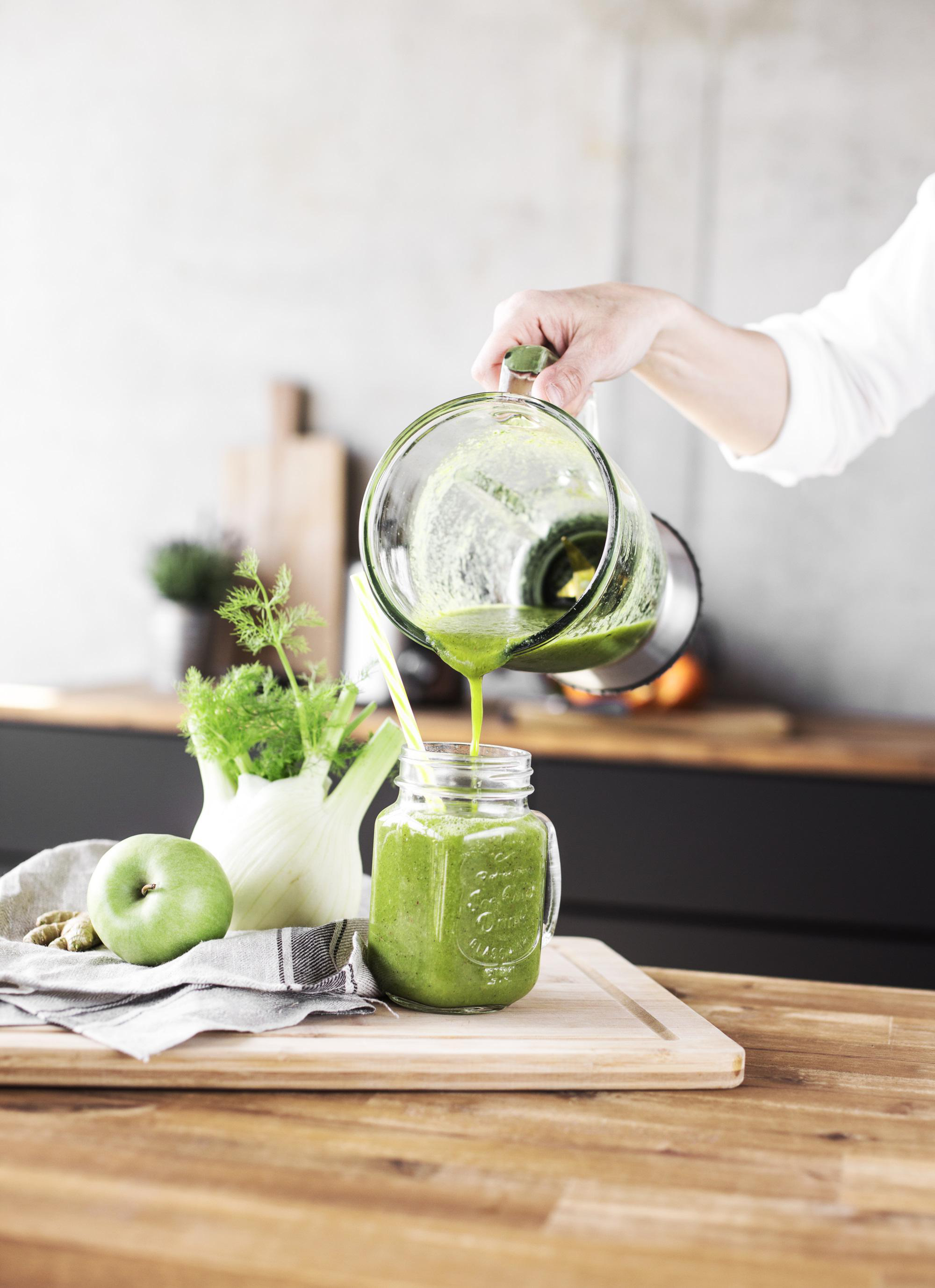 Eine Person gießt grünen Saft in ein Einmachglas.