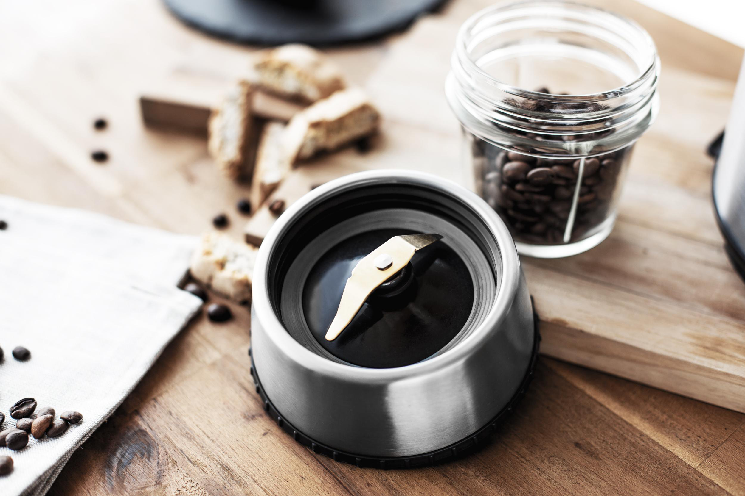 Kaffeemühlen-Teile auf Holzoberfläche, mit Kaffeebohnen und Biscotti.