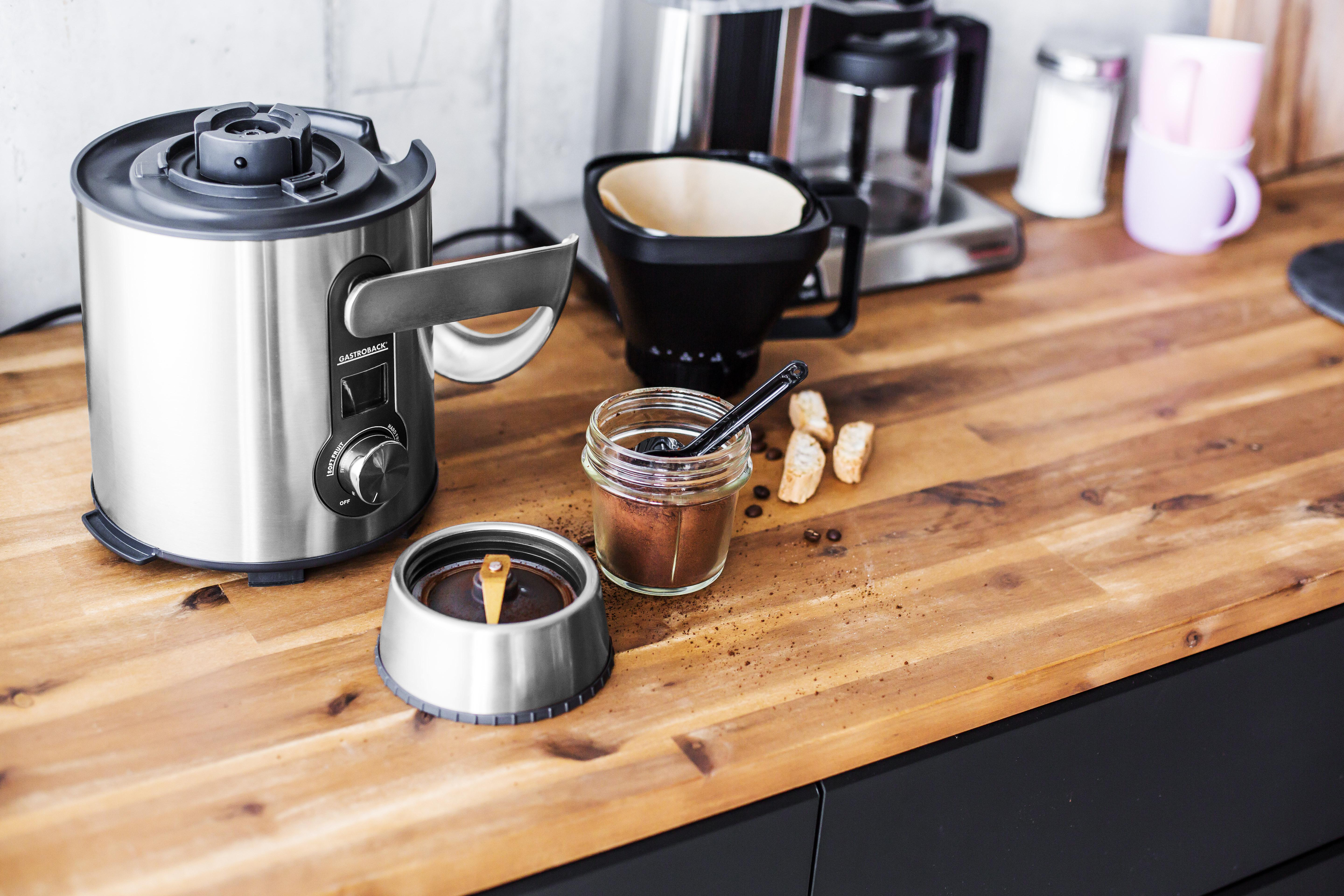 Kaffeemühle, Kaffeepulver, Filter und Kaffeemaschine auf einer Holz-Arbeitsplatte.