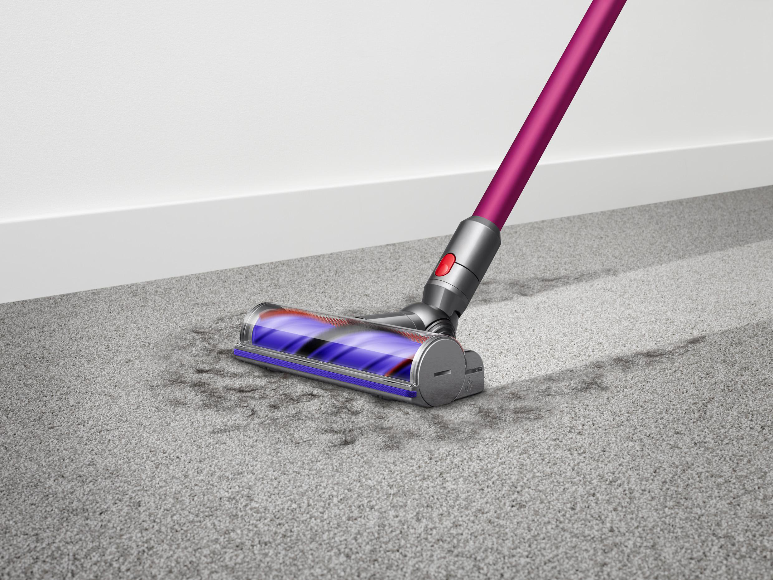 Ein lila-grauer Staubsauger reinigt einen grauen Teppich.
