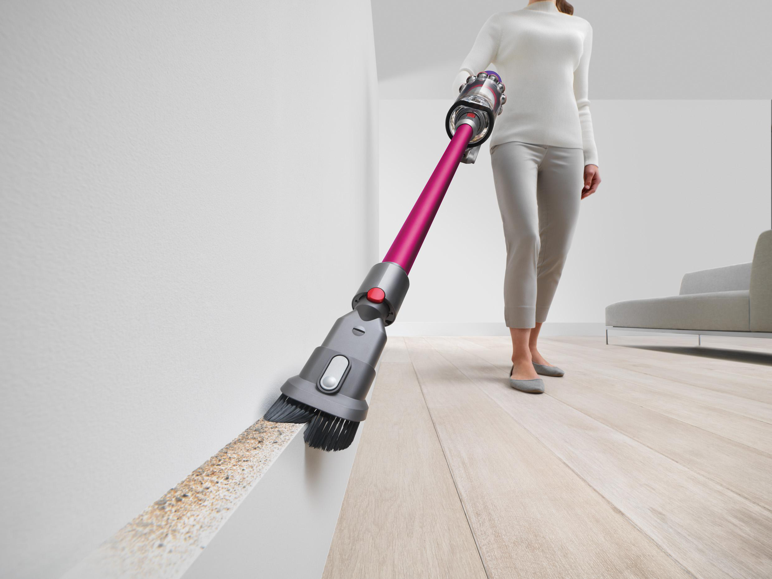 Eine Frau, die den Rand einer weißen Wand mit einem pinkfarbenen und grauen Staubsauger absaugt.