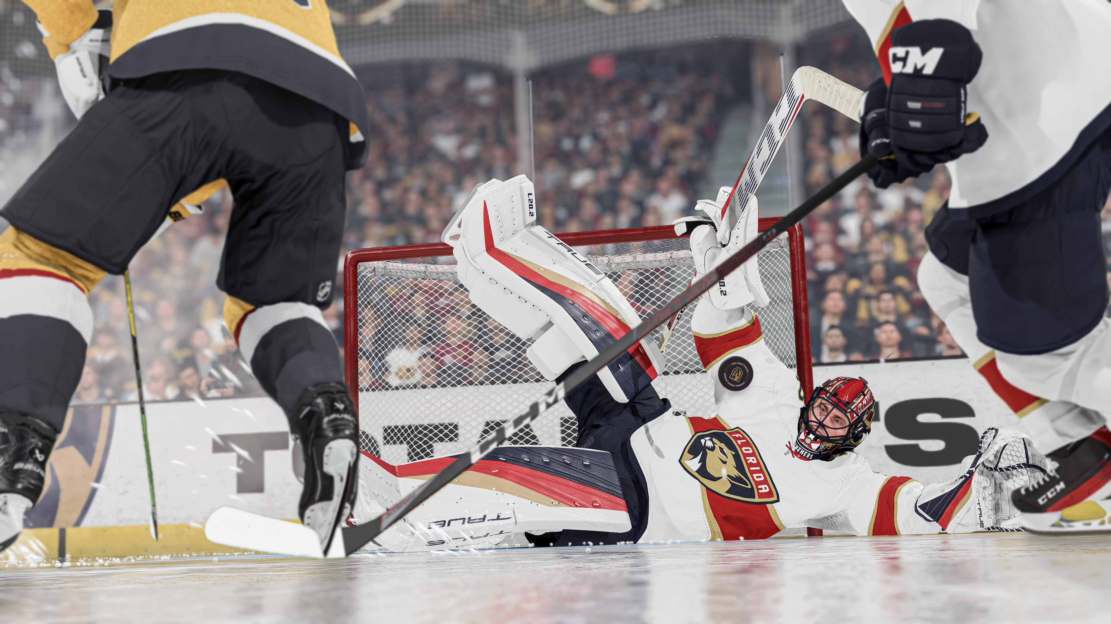 Ein Eishockey-Torwart in weiß-roter Ausrüstung liegt auf dem Eis und blockt einen Schuss, Spieler sichtbar.