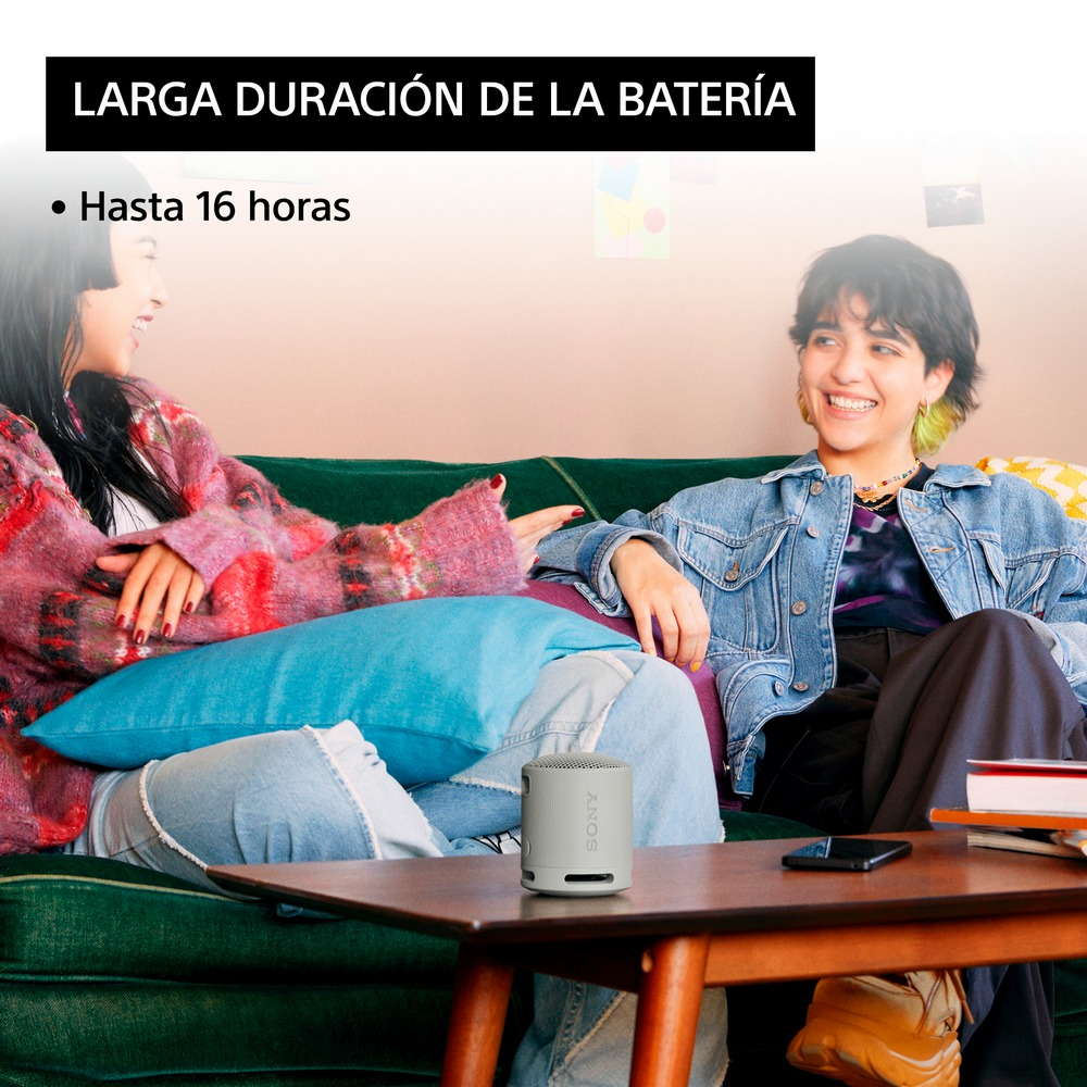 Dos mujeres en un sofá, una con un altavoz portátil. Texto dice 'Batería de larga duración, hasta 16 horas'.