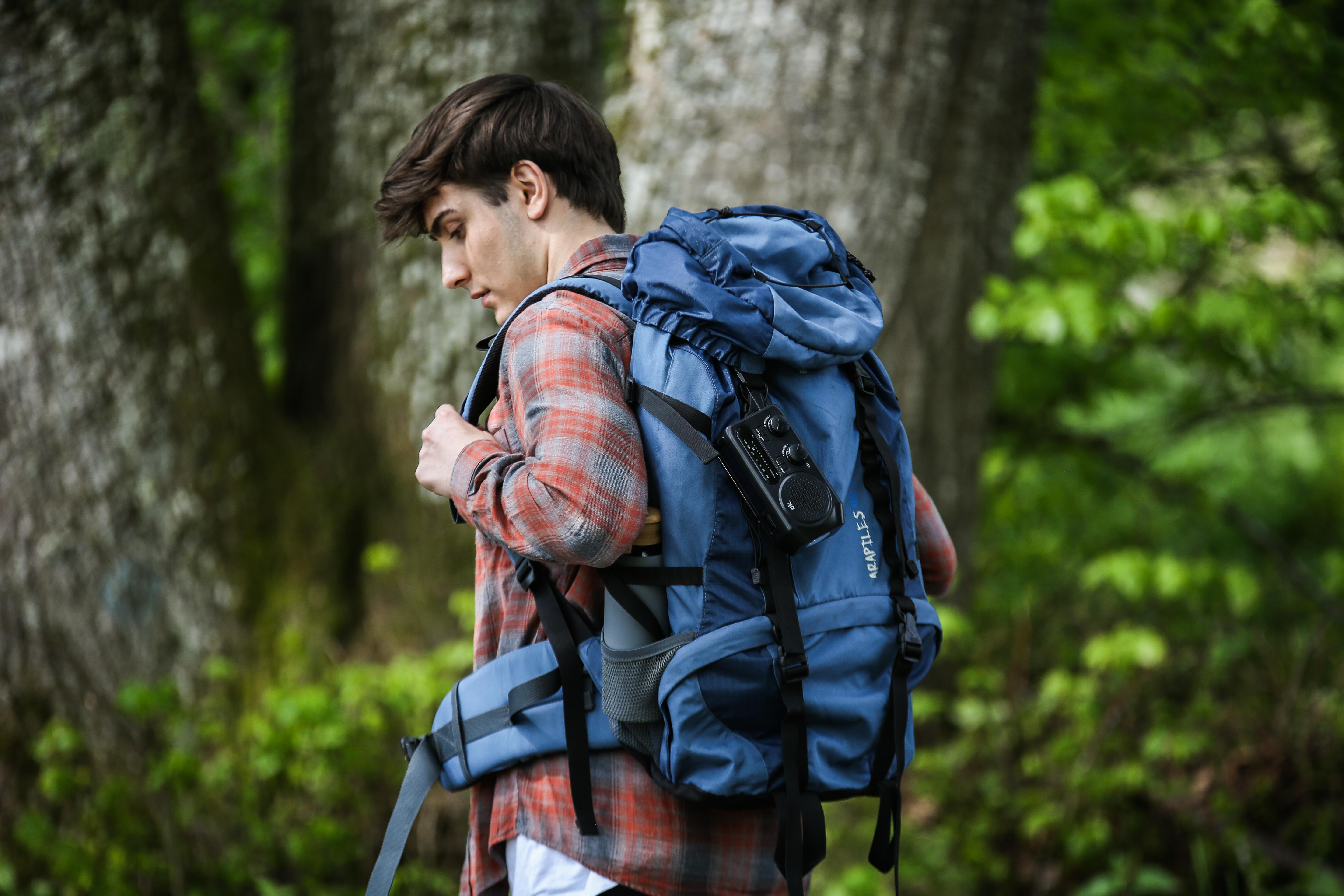 Ein Mann mit Rucksack geht im Wald, mit einem Radio auf der Tasche.
