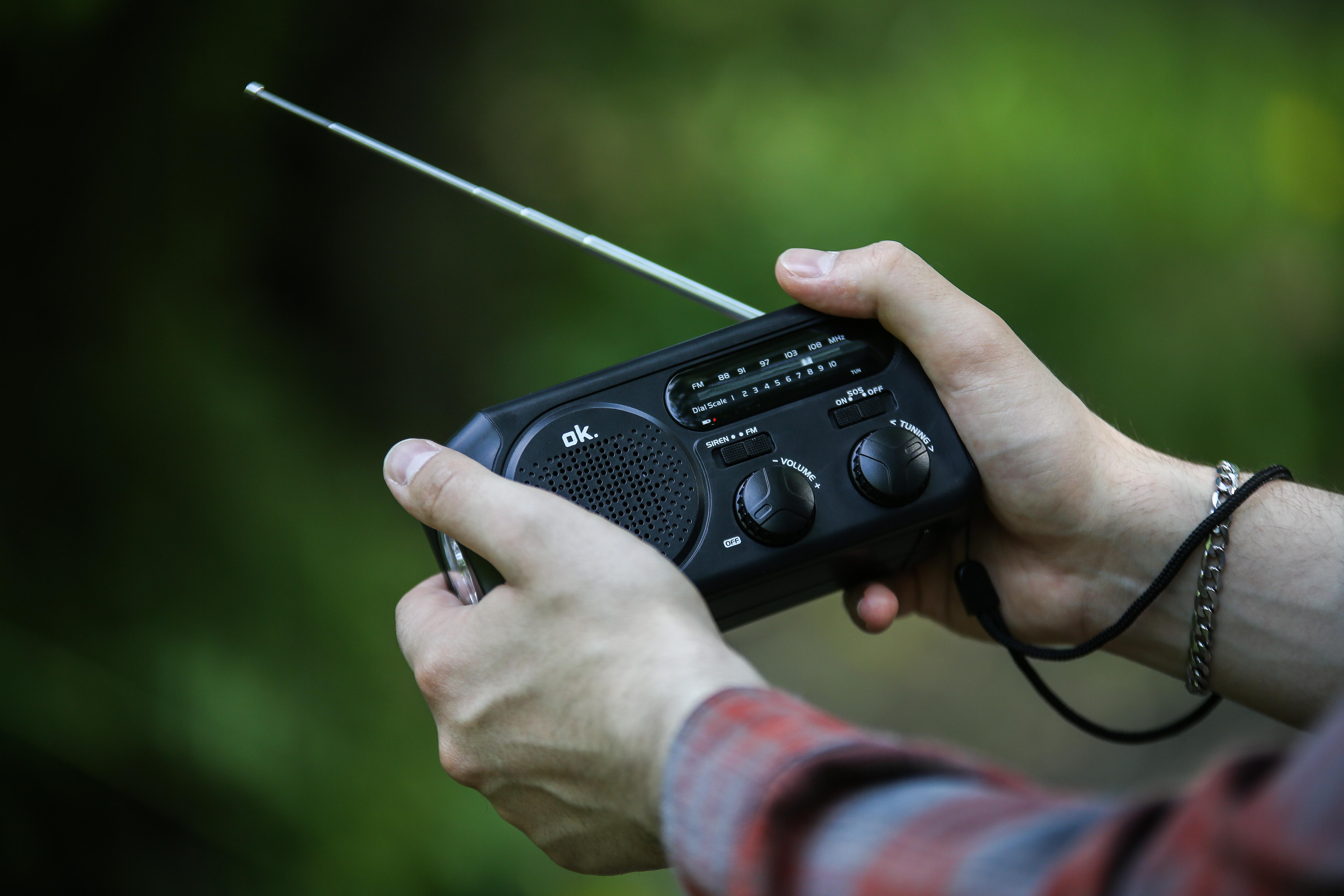 Hände halten ein schwarzes Radio, verschwommener grüner Hintergrund.