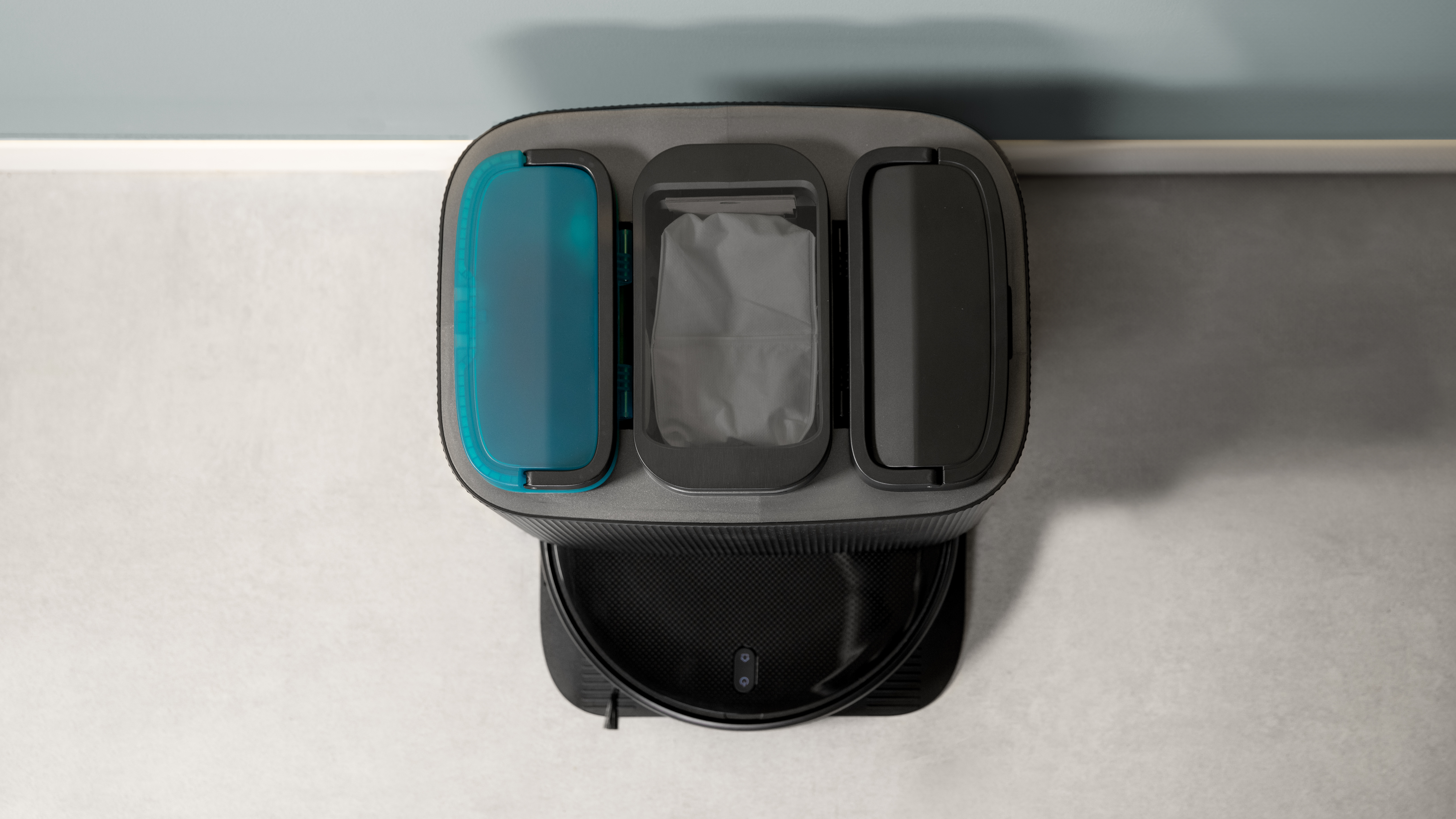 Vista superior de un robot aspirador con tres compartimentos y una base de carga.