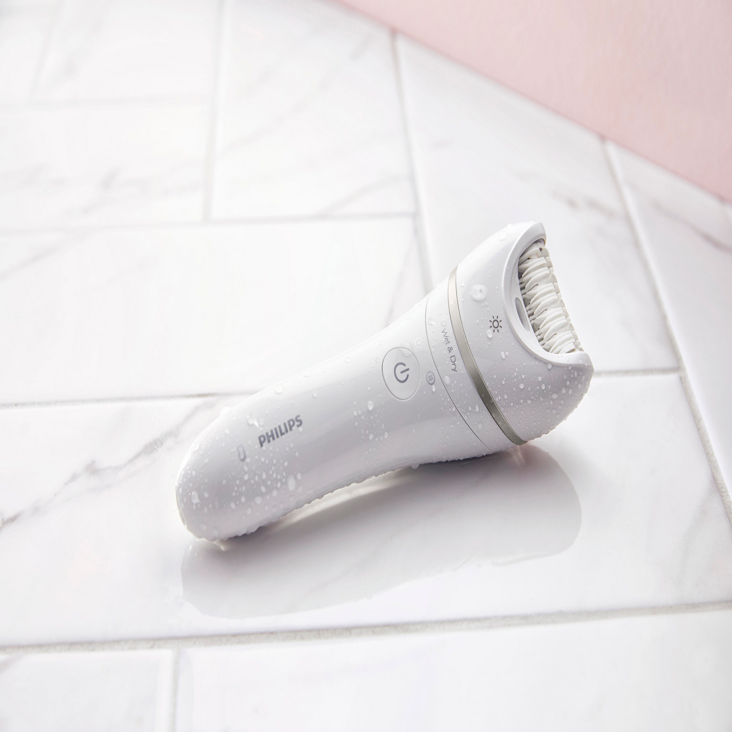 Witte Philips epilator met waterdruppels op een betegeld oppervlak.