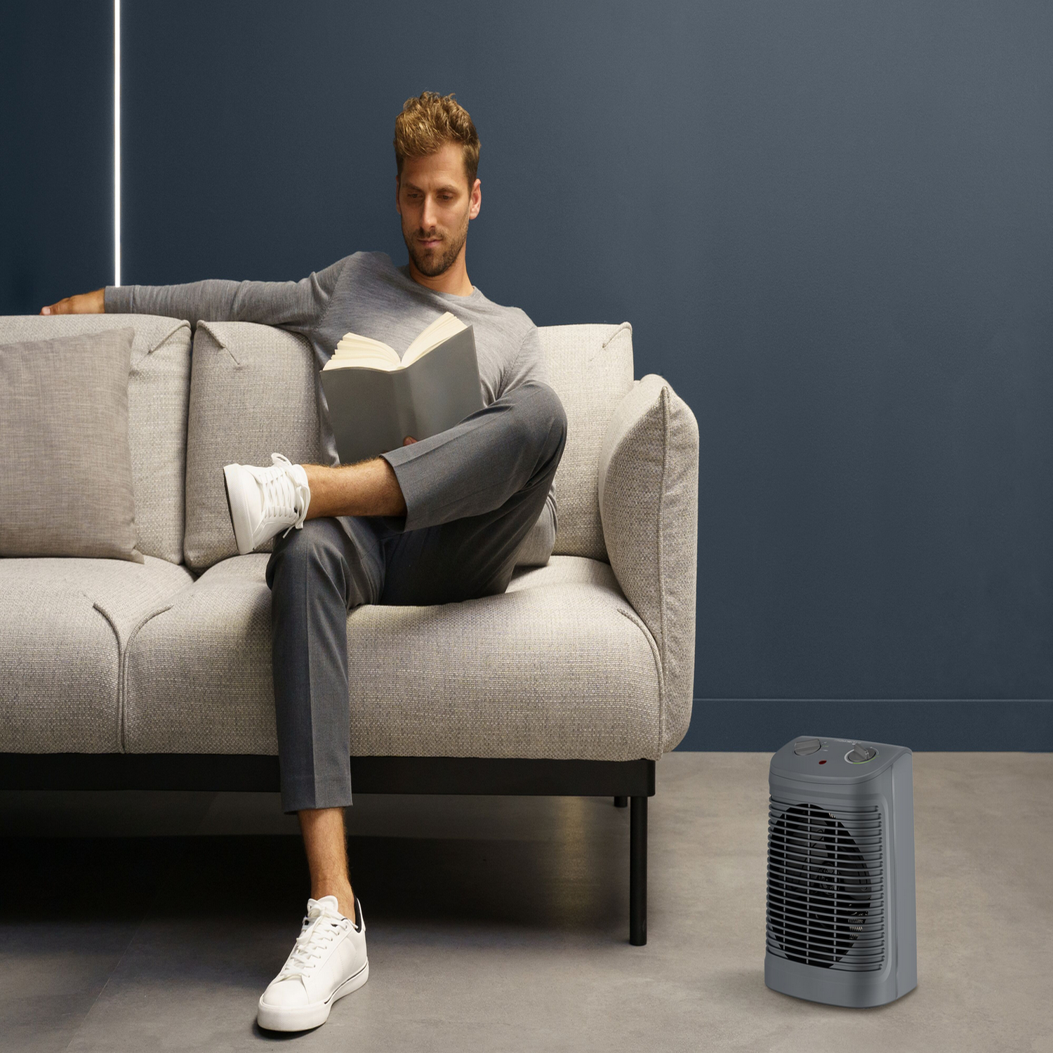 Man reading a book on a sofa near a heater.